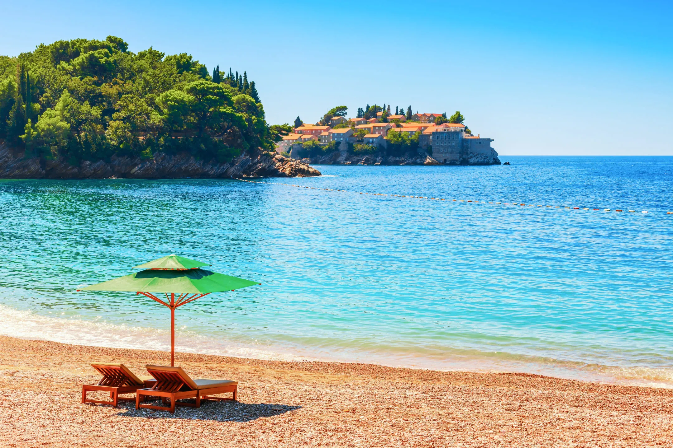 Two wooden sun loungers under a green umbrella on the seashore